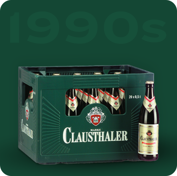 A green plastic crate contains multiple bottles of non-alcoholic beer from the 1990s.