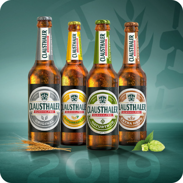 Four bottles of non-alcoholic beer are displayed against a teal background with a light hop graphic. Each bottle has a different colored cap and label.